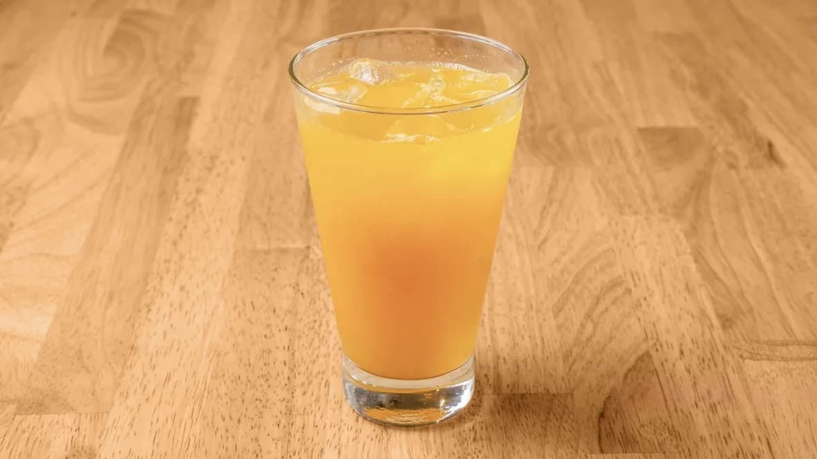 Tall glass of orange juice with ice on a light wood table