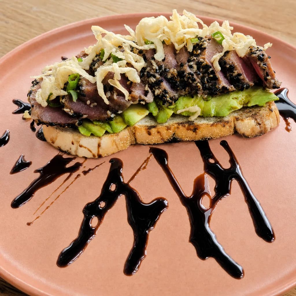 Tuna Love Toast with sesame-crusted seared tuna, avocado, crispy onion and balsamic drizzle