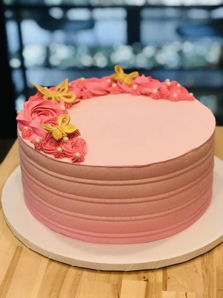 Pink celebration cake decorated with buttercream flowers and butterflies
